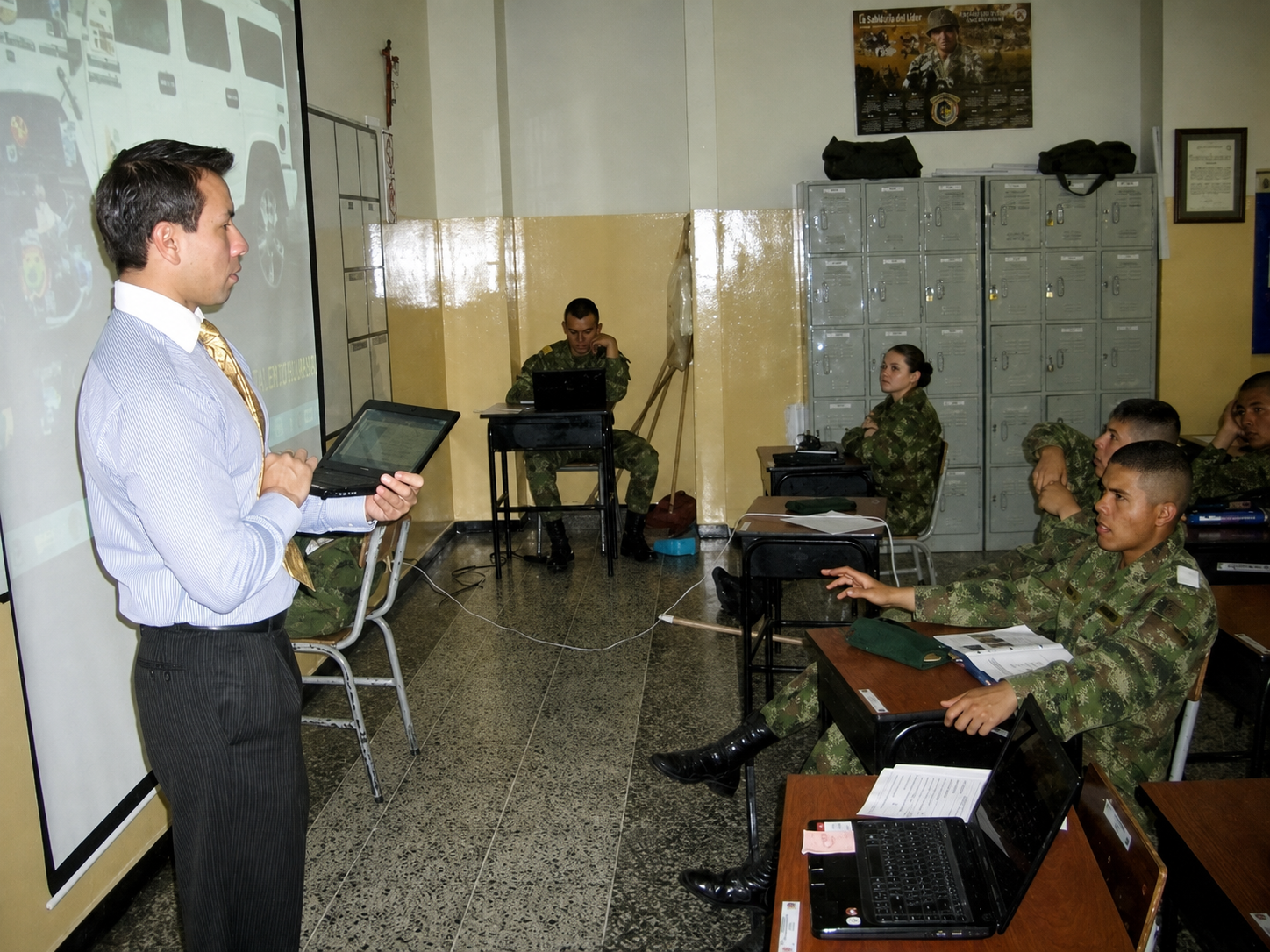 John teaching English in a classroom with a tablet and projected lesson.